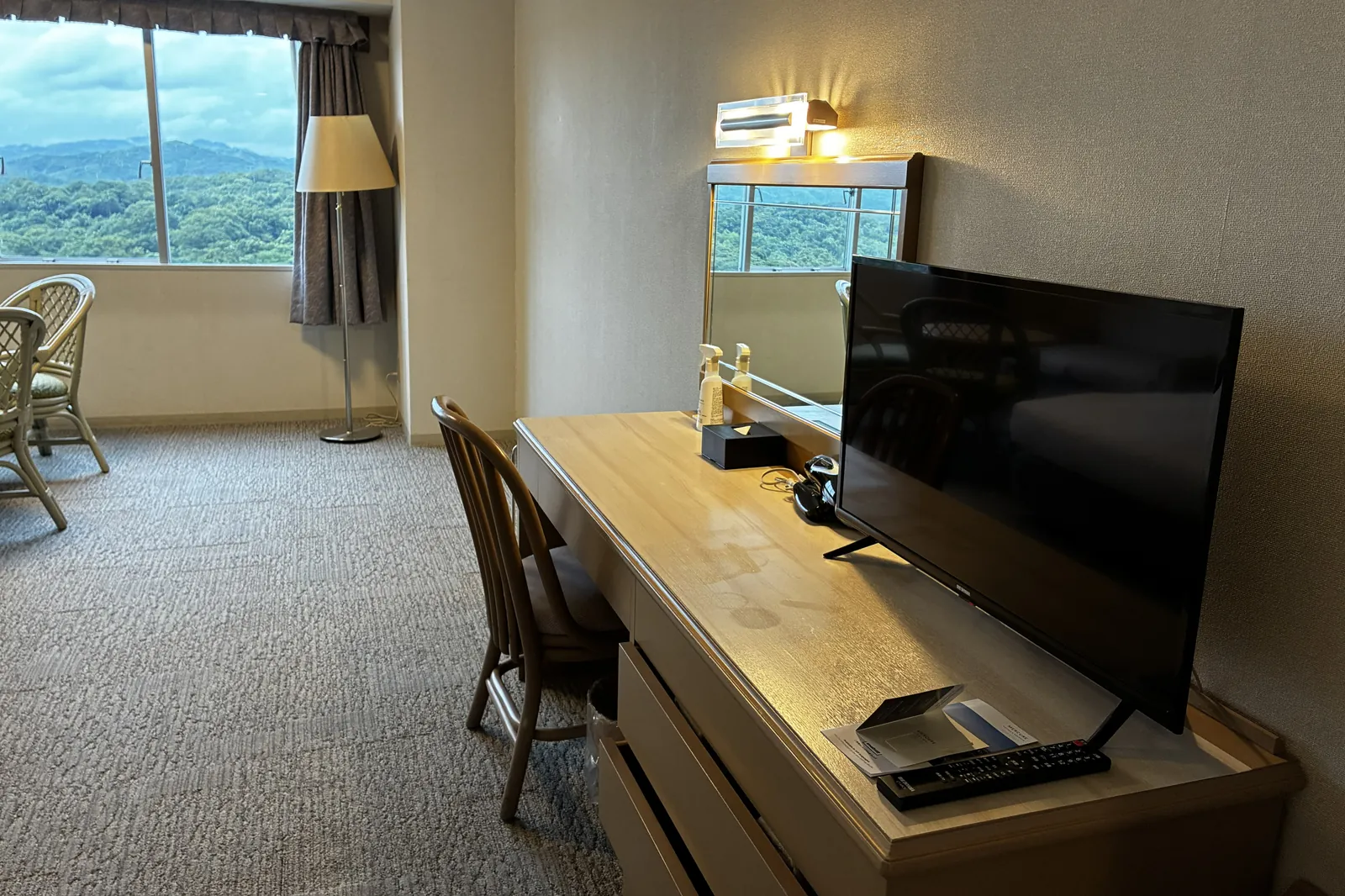 客室のデスクとテレビ。鏡に窓の外の緑が映っている