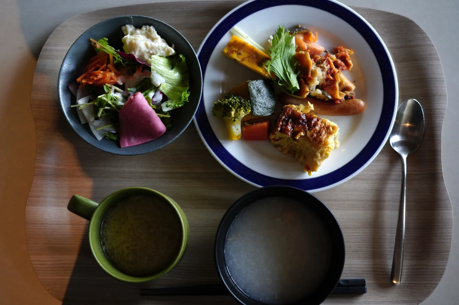 朝食のトレー。サラダ、野菜料理、キッシュ、ソーセージ、スープ、お粥